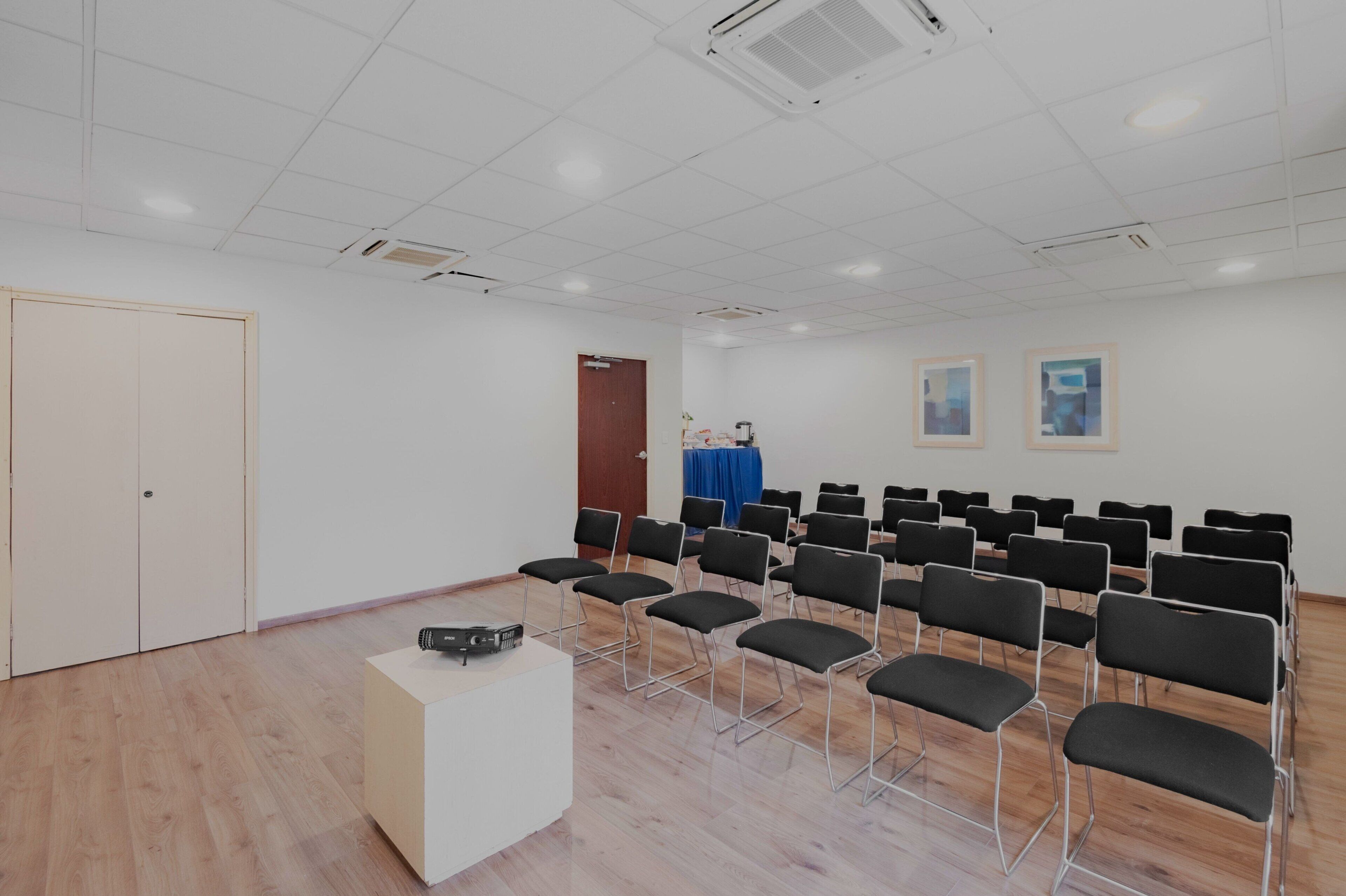A conference room with rows of chairs, a podium, and a door.