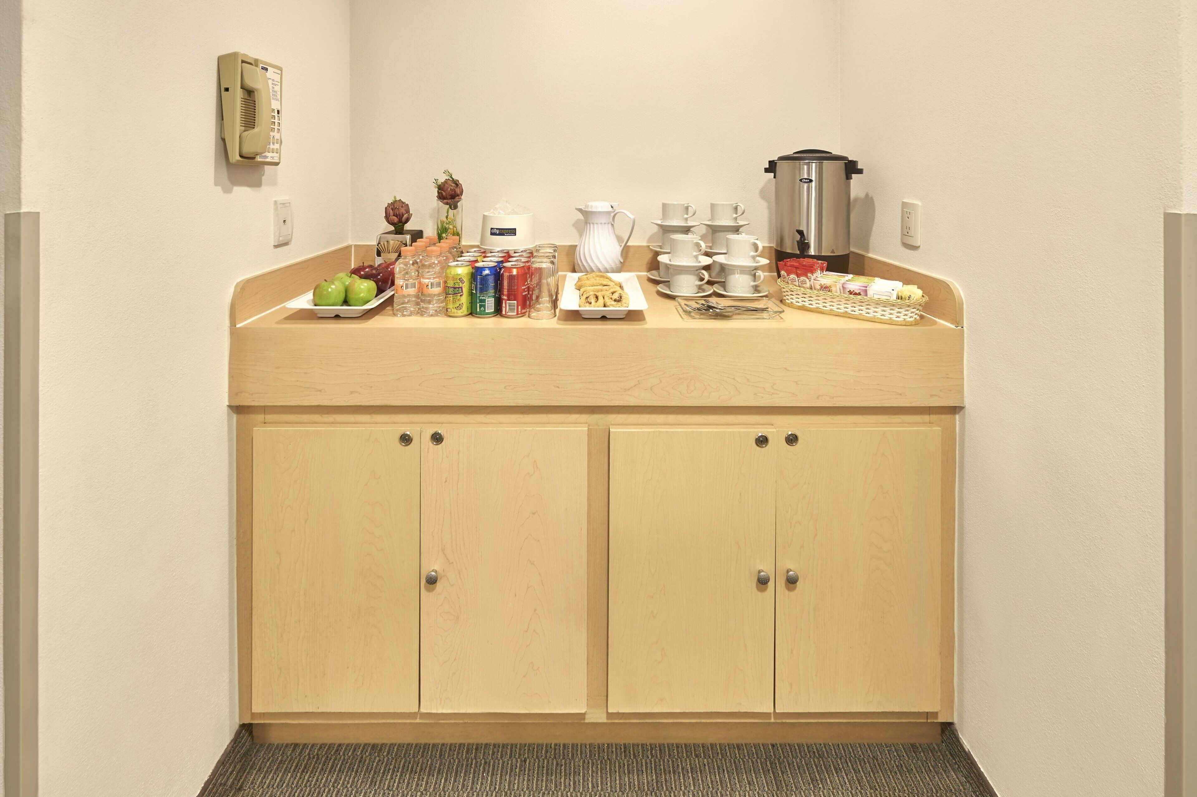 A kitchenette with a wooden countertop, a coffee maker, a kettle, and various food items.