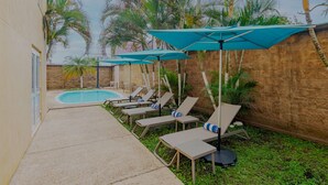 A poolside area with lounge chairs and umbrellas, a brick wall, and palm trees. - City Express by Marriott Minatitlan (Minatitlán)