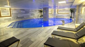 An indoor swimming pool with clear water, surrounded by lounge chairs and a tiled floor. - Buyuk Velic Hotel (Gaziantep)