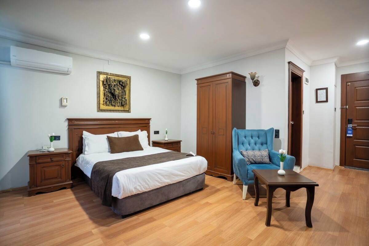 A bedroom with a bed, a nightstand, a wardrobe, a blue armchair, and a small table.
