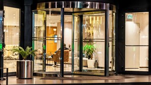 L’entrée d’un hôtel, avec une porte tournante, des panneaux de verre et un pot de fleurs.