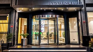 L’entrée d’un hôtel avec une façade en verre, une enseigne indiquant « HÔTEL LAMARTINE » et une porte tournante.