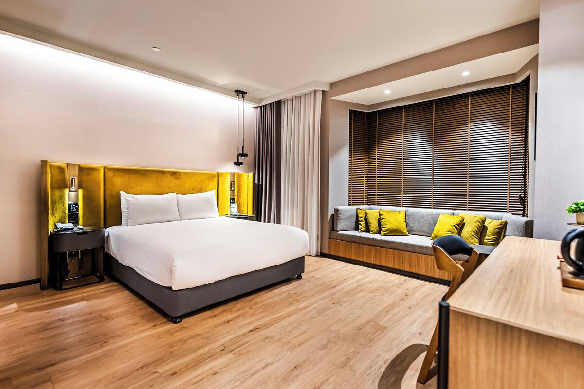 A modern hotel room with a large bed, a desk, and a window with blinds.