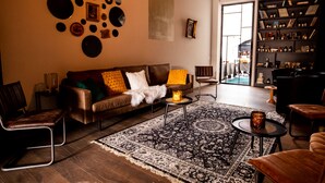 A modern living room with a brown leather sofa, a patterned rug, and a bookshelf filled with books and decorative items. - Hotel Den Grooten Wolsack (Mechelen)