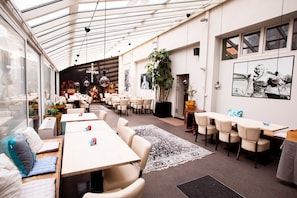 A spacious indoor area with multiple tables and chairs, a large plant, and artwork on the walls. - Hotel Den Grooten Wolsack (Mechelen)