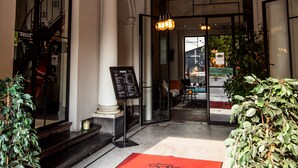 A hotel entrance with a red carpet, columns, a chandelier, and a menu sign. - Hotel Den Grooten Wolsack (Mechelen)