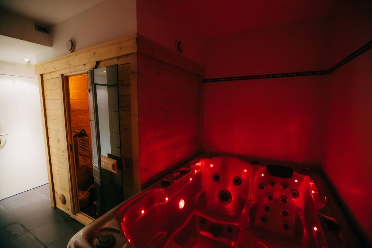 A red-lit room with a wooden door, a glass shower enclosure, and a bathtub with multiple jets.