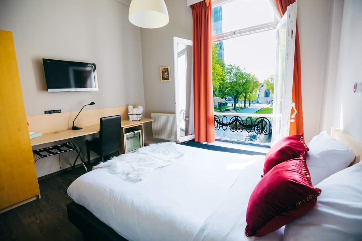 A hotel room with a bed, a desk, a chair, a TV, and a window with curtains.