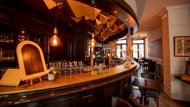 A bar area with a curved counter, hanging light fixtures, and a wooden display. - Hotel Den Grooten Wolsack (Mechelen)