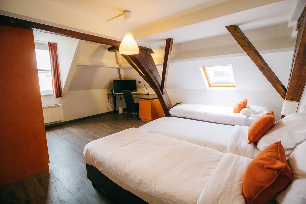 A bedroom with two beds, wooden beams, a desk, and a window.