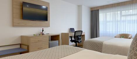 A hotel room with two beds, a desk with a chair, a television mounted on the wall, and a window with curtains.