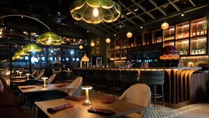 L’intérieur d’un restaurant, avec des tables, des chaises, des lampes suspendues et un bar doté d’étagères remplies de bouteilles.