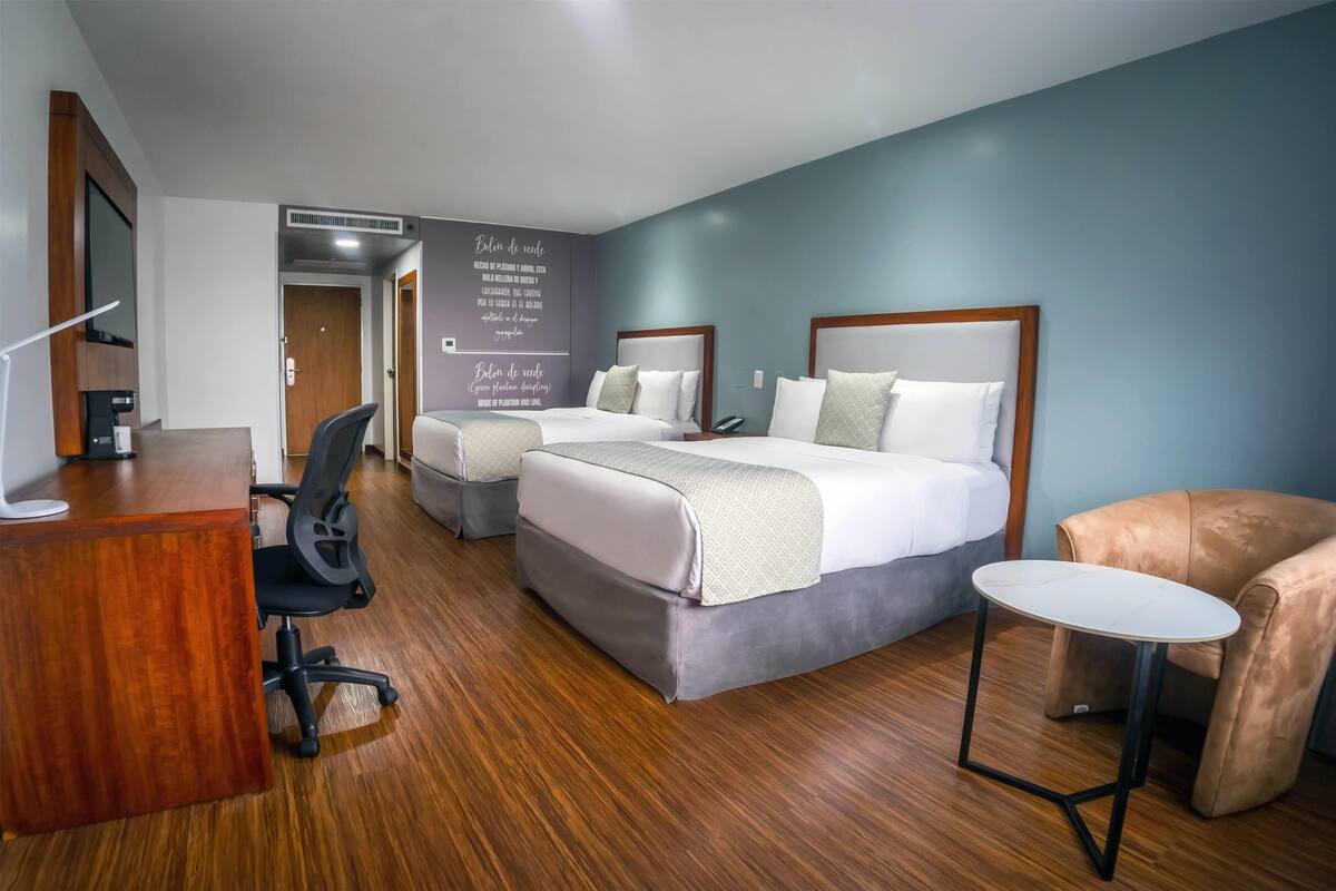 Ein Hotelzimmer mit zwei Betten, einem Schreibtisch, einem Stuhl und einem kleinen Tisch.