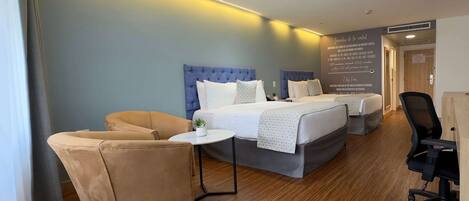 Habitación de hotel con dos camas, un sofá, una mesita y una silla.