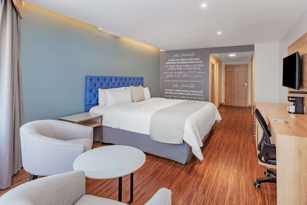 Ein modernes Hotelzimmer mit einem großen Bett, einem Schreibtisch, einem Stuhl und einem Fernseher.