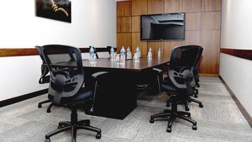 A conference room with a long table, four chairs, a flat-screen TV, and water bottles on the table.