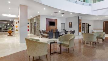 A modern hotel lobby with a reception desk, seating area, and a glass railing overlooking the interior.