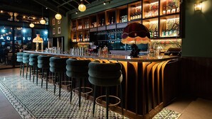 Un espace bar doté d’un long comptoir, de nombreux tabourets et d’étagères remplies de bouteilles.