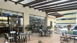 Un espace extérieur aménagé avec un design moderne, comprenant un mélange de canapés et de tables, et une entrée en verre donnant accès à un bâtiment.