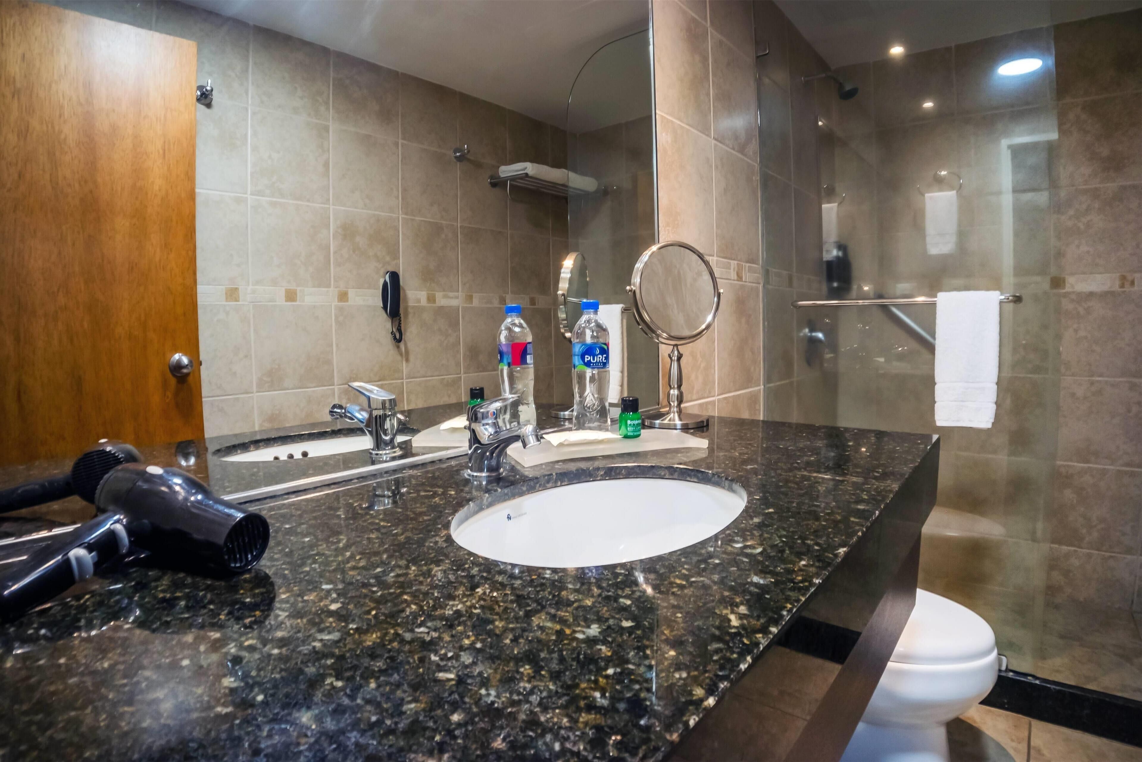 A bathroom with a granite countertop, a sink, a mirror, a towel rack, and a shower area.