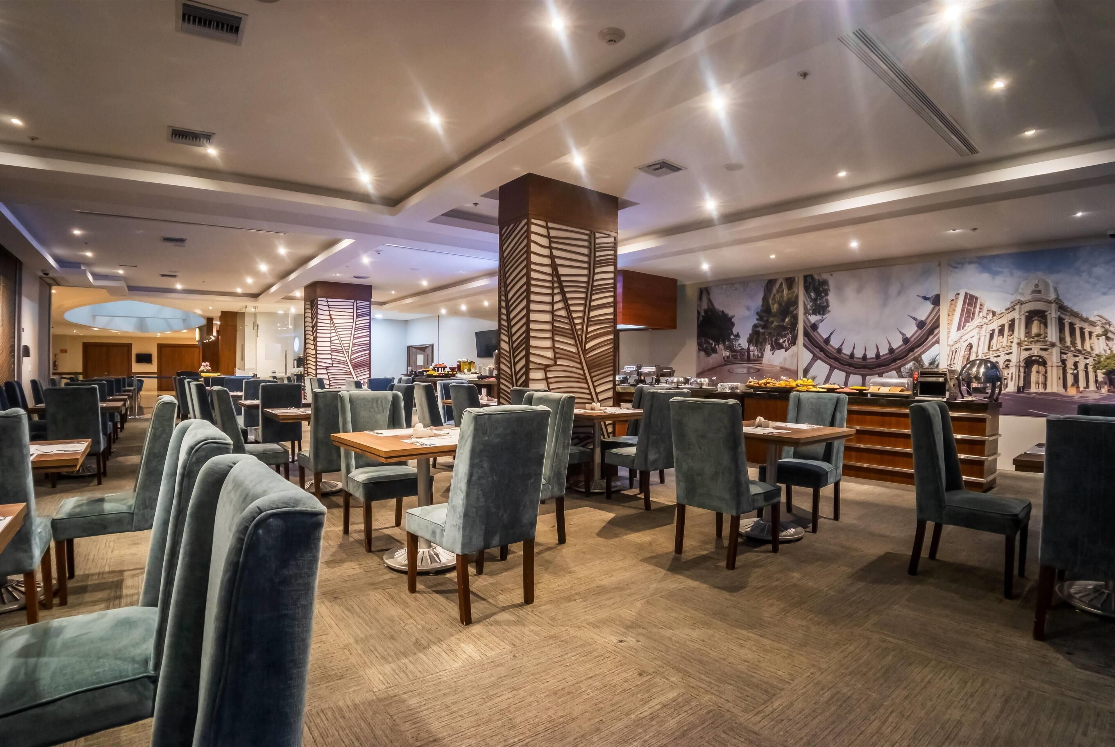 A spacious restaurant with high-backed chairs, a central bar area, and a mural of a cityscape.