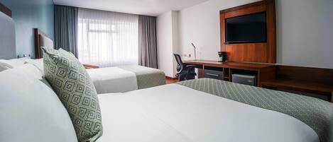 Habitación de hotel con dos camas, un escritorio, una silla, un televisor de pantalla plana y una ventana con cortinas.