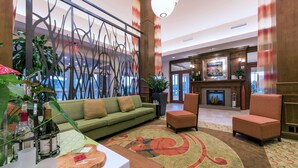 A lobby with a green sofa, two armchairs, a wooden table with a cutting board, and a decorative wall with abstract patterns.