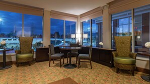 A hotel room with a large window, a round table, and four patterned chairs.