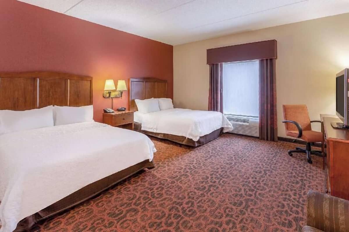 A hotel room with two beds, a desk, a chair, a TV, and a window with curtains.