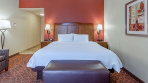 A hotel room with a large bed, a bench, a nightstand with a lamp, and a framed picture on the wall.