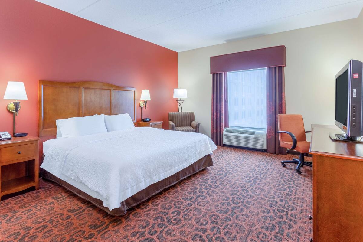A hotel room with a large bed, two bedside lamps, a desk with a computer, a chair, and a television.