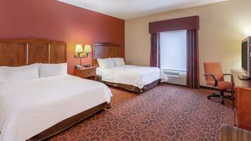 A hotel room with two beds, a desk, a chair, a TV, and a window with curtains.