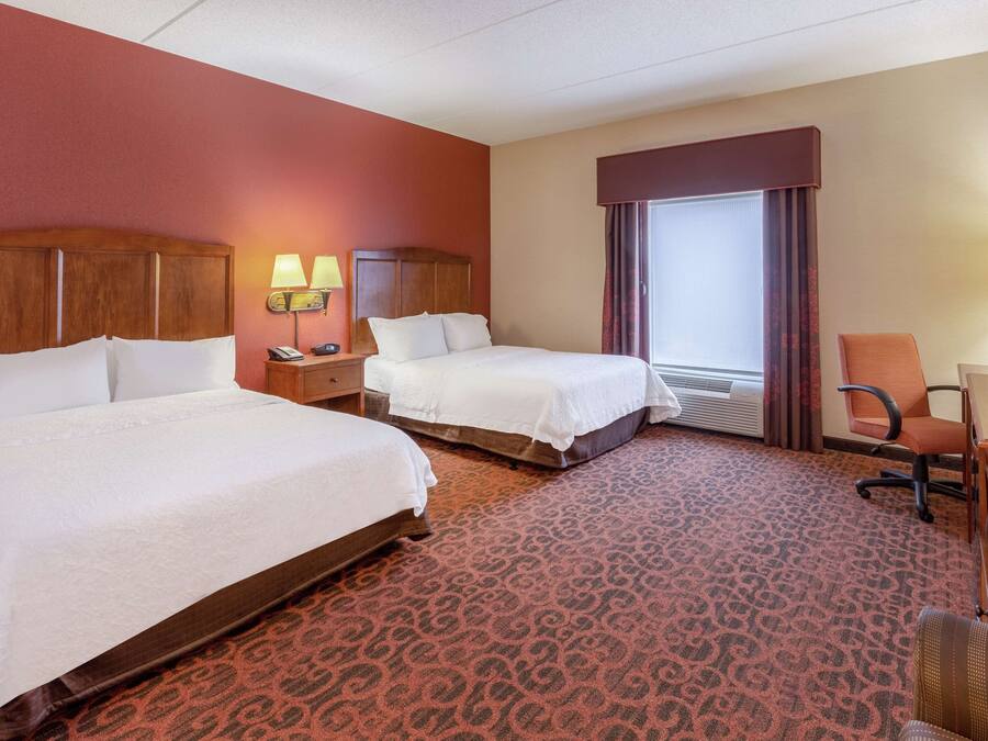 A hotel room with two beds, a desk, a chair, a TV, and a window with curtains.