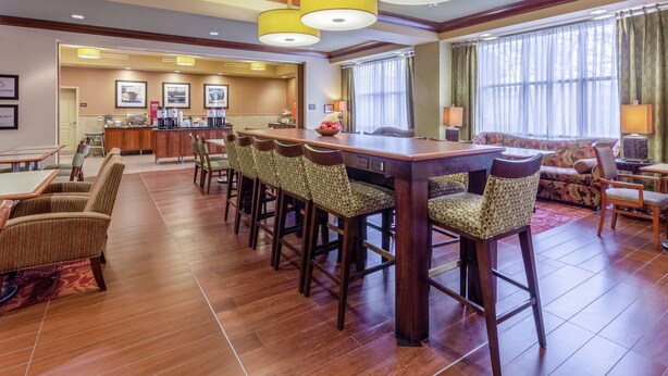A hotel lobby with a long bar, multiple seating areas, and a kitchen in the background.
