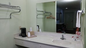 Un baño de hotel con un espejo grande, un lavamanos, un perchero para toallas y una cafetera sobre el mostrador.