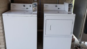 Dos lavadoras Whirlpool de carga frontal en un cuarto de lavado con paredes de ladrillo y piso de concreto.