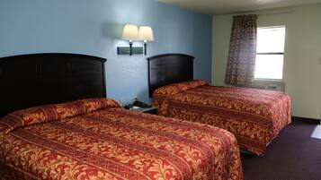 Une chambre avec deux lits, chacun recouvert d’une couvre-lit à motifs, une table de chevet avec une lampe et une fenêtre avec un rideau.