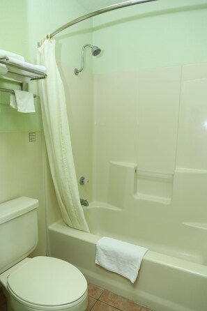 A bathroom with a toilet, a bathtub, and a shower curtain. - Budget Inn (Stephenville)