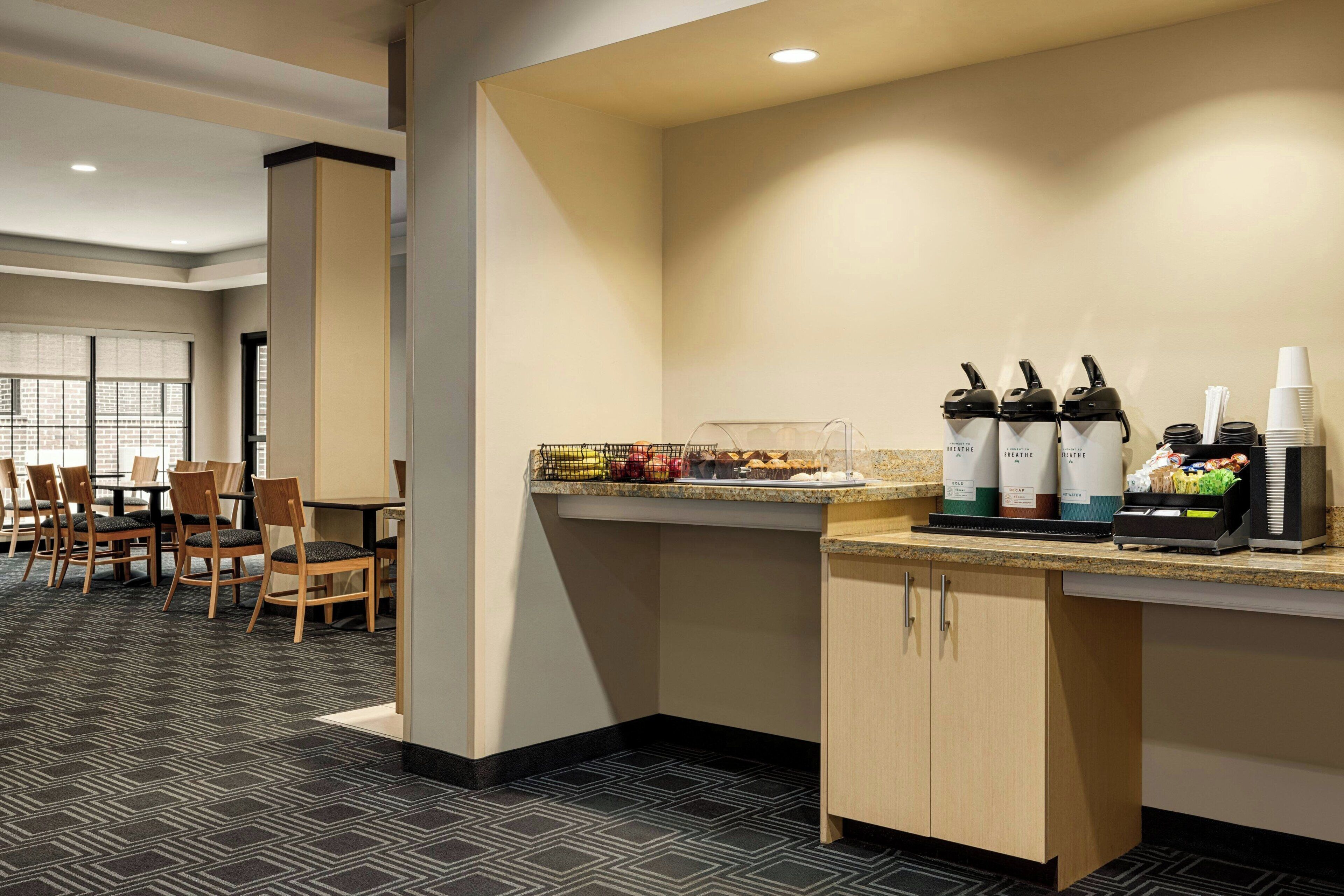 A hotel room with a kitchenette, a dining area with chairs and a table, and a window with blinds.