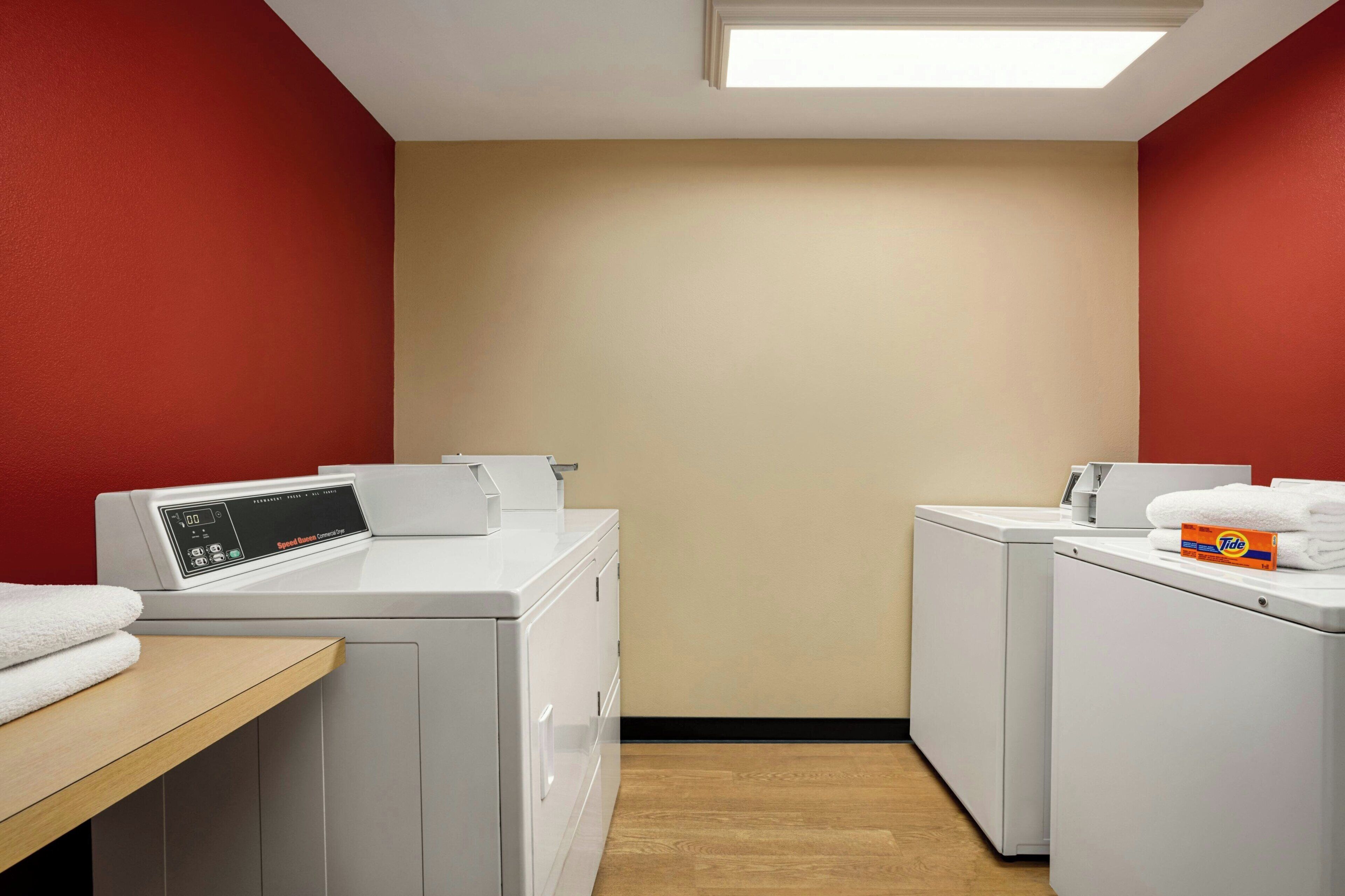 A laundry room with two white washing machines, a wooden bench, and a red wall.