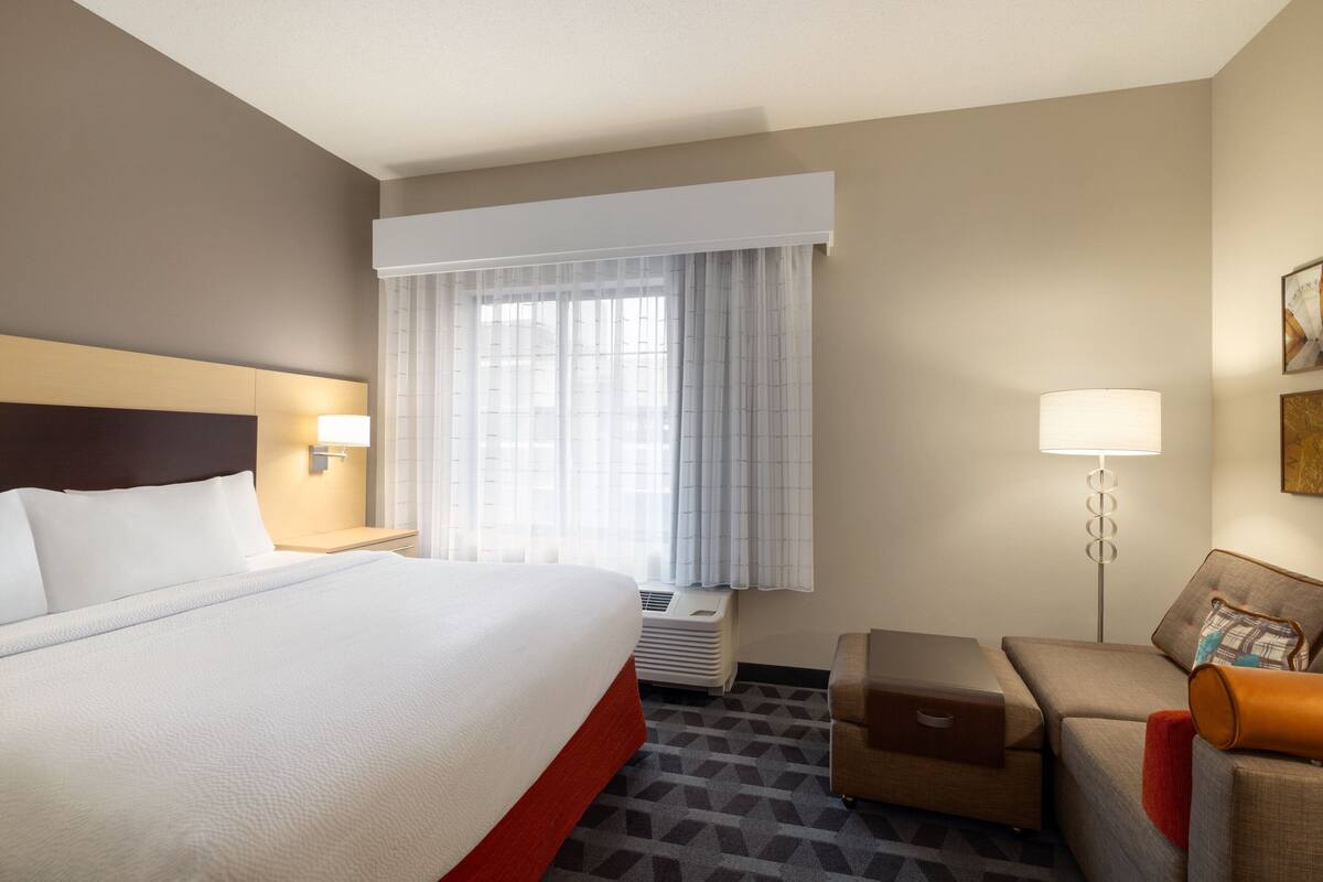 A hotel room with a large bed, a desk with a lamp, a sofa, and a window with curtains.