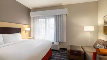 A hotel room with a large bed, a desk with a lamp, a sofa, and a window with curtains.