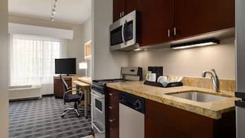 A compact hotel kitchen with a microwave, stove, sink, and a small dining area with a chair and table.