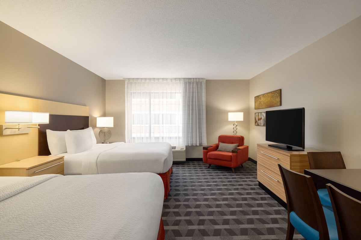 A hotel room with two beds, a TV, a desk, and a chair.