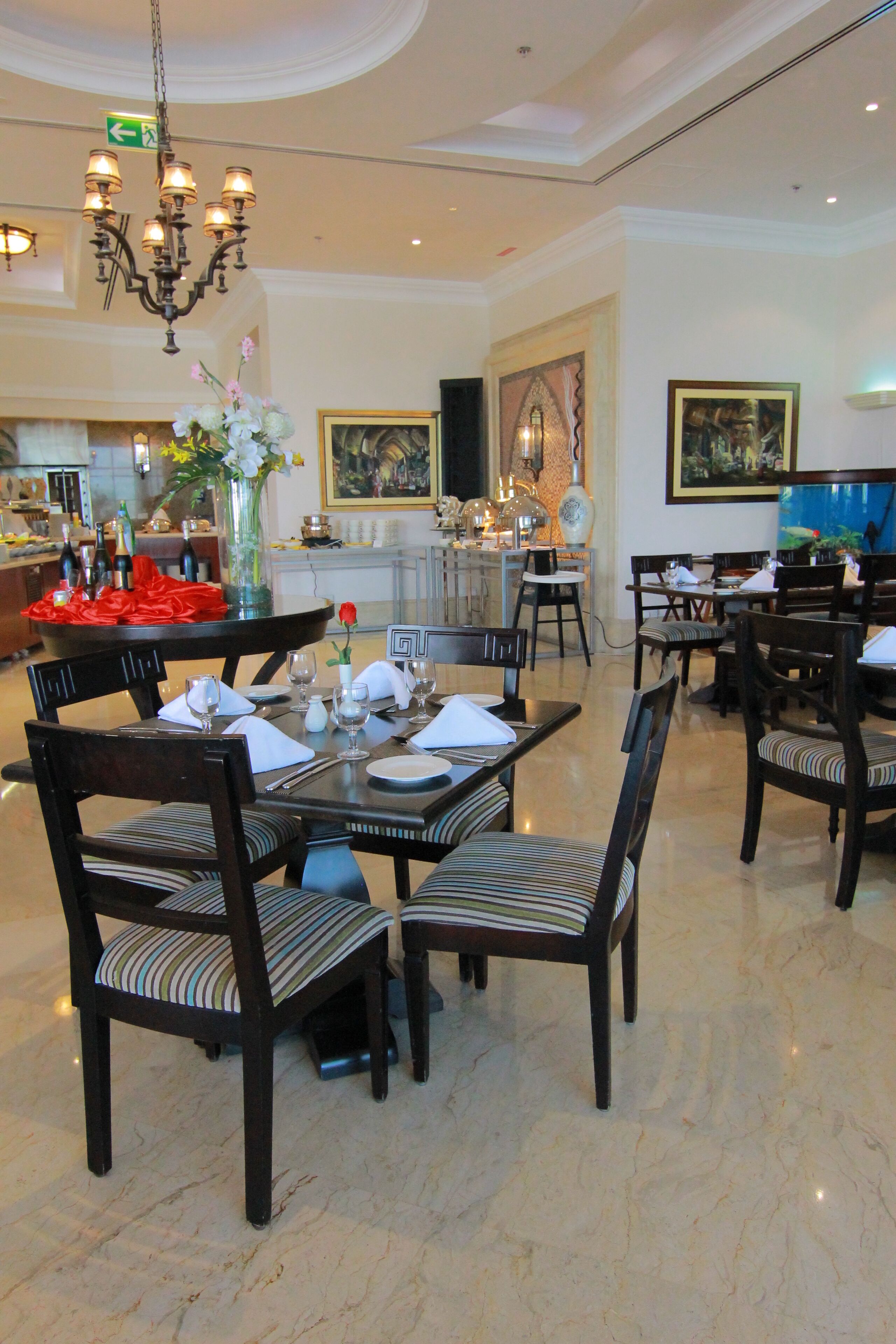 A dining area with a chandelier, tables set for four, and chairs with striped cushions.