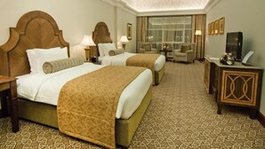 A hotel room with two beds, a sitting area, a television, and a desk with a lamp. - Ayla Hotel  (Al Ain)