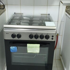 Une cuisine équipée d’une cuisinière et d’un four, avec des murs recouverts de carreaux blancs et une conduite de gaz visible.