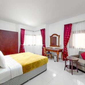 A hotel room with a bed, a desk, a chair, a sofa, and a small table.