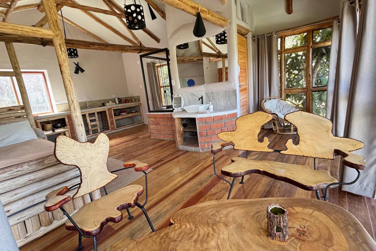 A rustic interior with exposed wooden beams, a brick fireplace, and a wooden dining table with chairs.